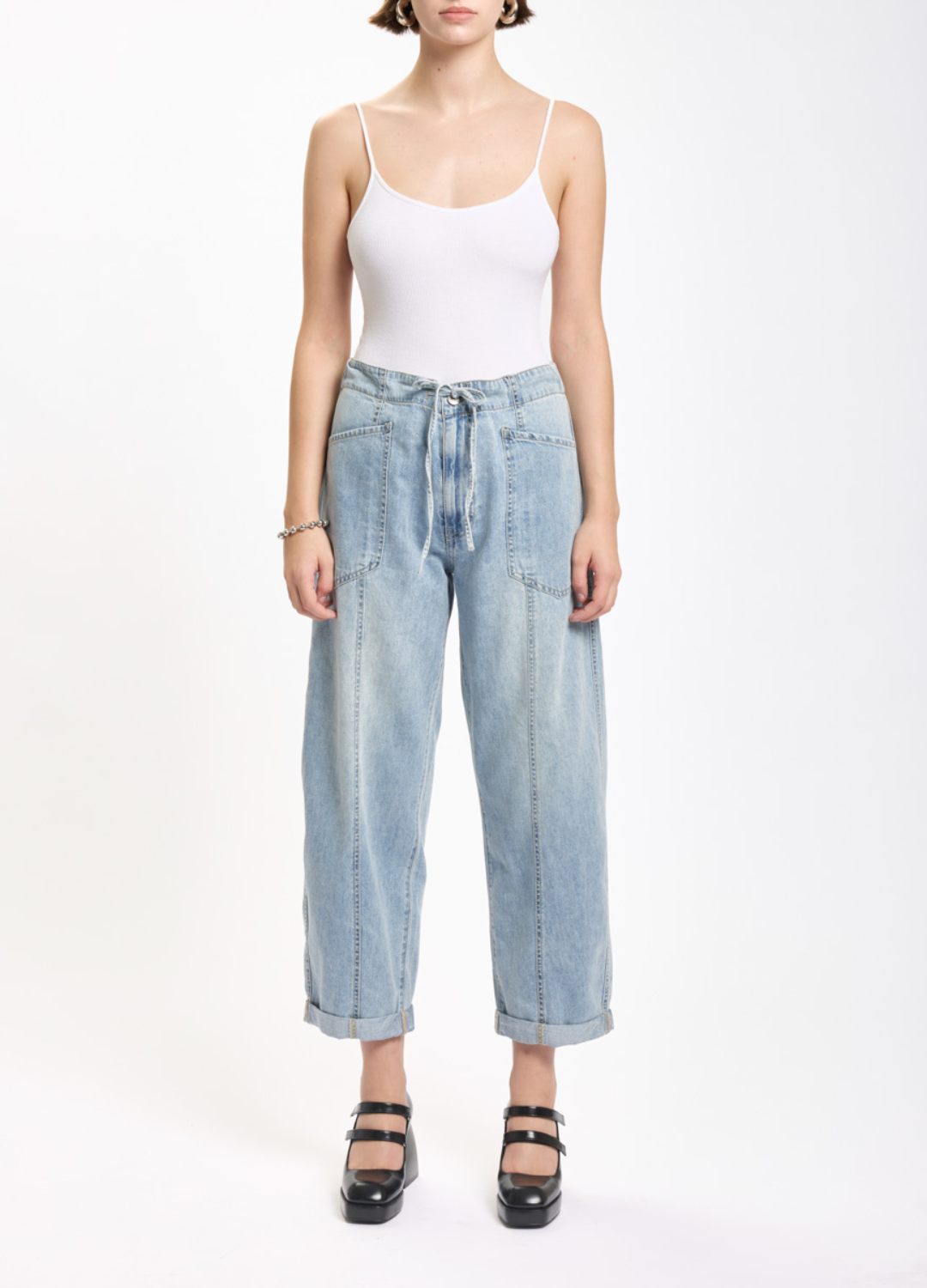 Person wearing a white tank top and light blue jeans on a white background
